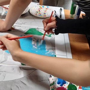 Na zdjęciu przybliżenie na malujace ręce dzieci. jedno z nich maluje jezioro