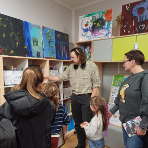 Zdjęcie przedstawia uczestników wernisażu, którzy w skupieniu słuchają prowadzącego.