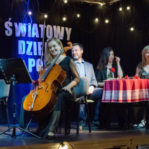 Na pierwszym planie widoczna jest uśmiechnięta wiolonczelistka a w kadrze dostrzec można również altowiolistkę – obie artystki emanują pozytywną energią i radością ze wspólnego występu.  W tle, przy stoliku, siedzą trzej aktorzy torzymskiego teatru, tworząc spokojne, kameralne dopełnienie sceny i podkreślając artystyczny charakter wydarzenia.