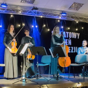 Na zdjęciu widoczni są wszyscy muzycy, stojący na scenie po zakończeniu utworu. W tle, przy stoliku, siedzą aktorzy, którzy nagradzają ich występ brawami. Całość oddaje moment uznania i podziękowania za wspólne, pełne emocji artystyczne przeżycie.