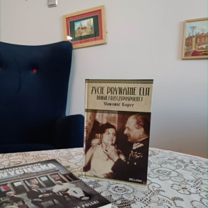  Na stoliku stoi książka pt. "Życie prywatne elit Drugiej Rzeczpospolitej" S. Kopera