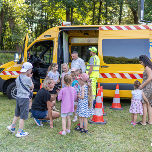 Punkt przygotowany przez Autostradę Eksploatacja S.A. – dzieci z zainteresowaniem słuchają informacji dotyczących bezpieczeństwa podczas podróży. W tle widoczny jest charakterystyczny żółty pojazd patrolowy Autostrady Eksploatacja S.A.