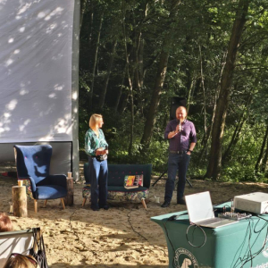 Wojciech Chmielarz i dyrektor Biblioteki witają przybyłych czytelników na plaży, na tle lasu nad Jeziorem Jasnym.